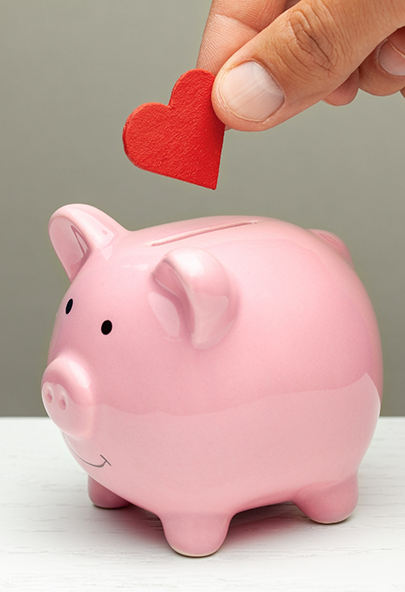 Hand placing a red paper heart in a pink piggy bank