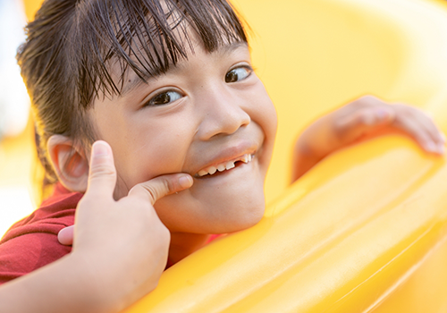 Child with a few missing teeth pointing to their smile
