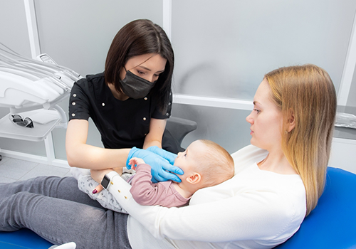 Baby receiving a dental exam while laying in their mother's lap