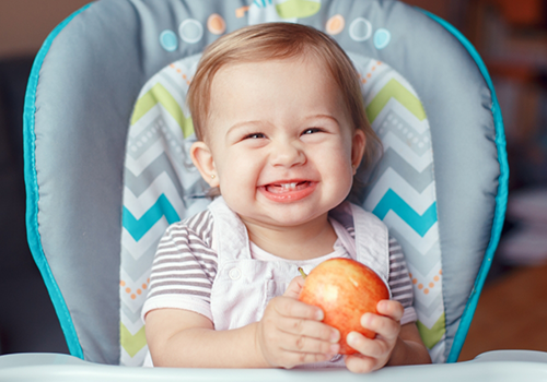 Baby grinning while holding a red apple