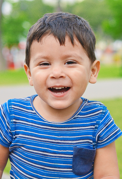 Young boy grinning outside after seeing his dentist for toddlers in Bakersfield