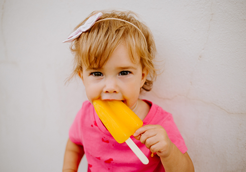 Toddler girl eating an orange popsicle