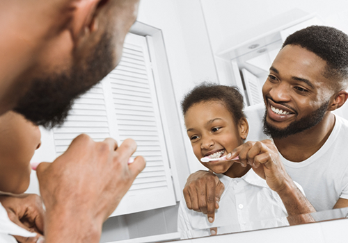 Father showing his young son how to brush his teeth