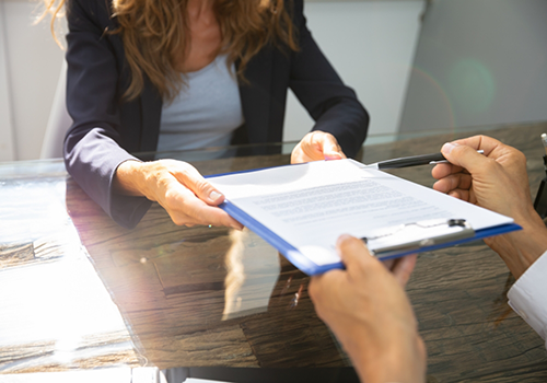 Woman handing a clipboard with paperwork to someone across a table