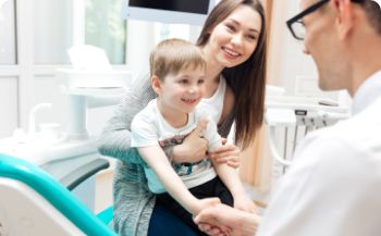 Young boy shaking hands with his dentist while his mother holds him