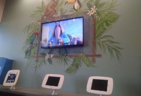 Three small touchscreens set up in front of a larger screen mounted on the wall