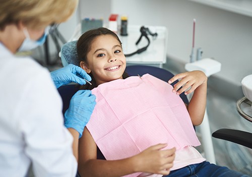 Child smiling while dentist puts on pink bib 