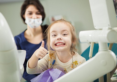 Child smiling while giving thumbs up in treatment room