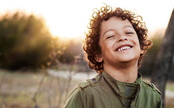 Young boy with curly brown hair grinning in the sun