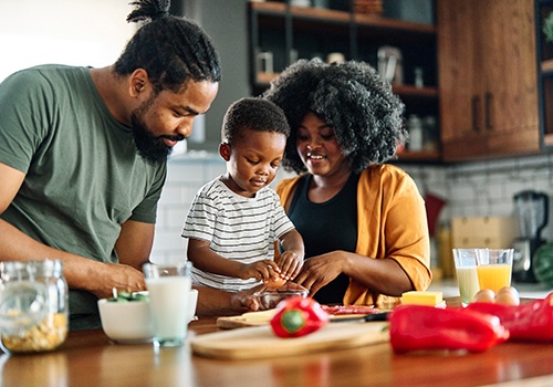 Man, woman, and little boy making breakfast with eggs, milk, orange juice, and peppers on the counter