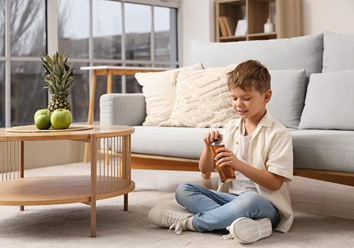 Boy sitting cross-legged in front of sofa struggling to open a bottle