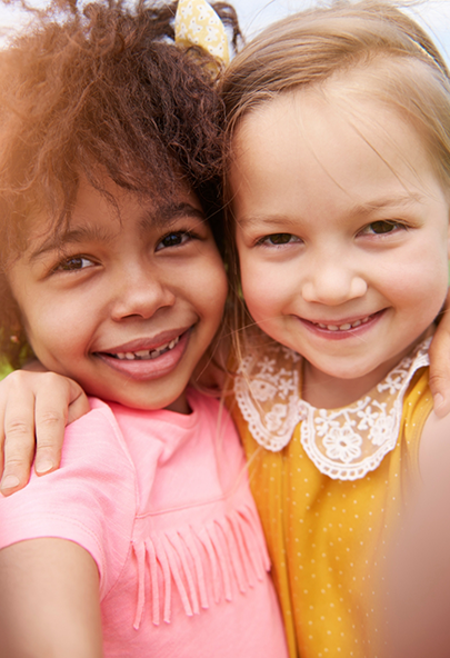 Two young girls grinning together after seeing their pediatric dentist in Bakersfield