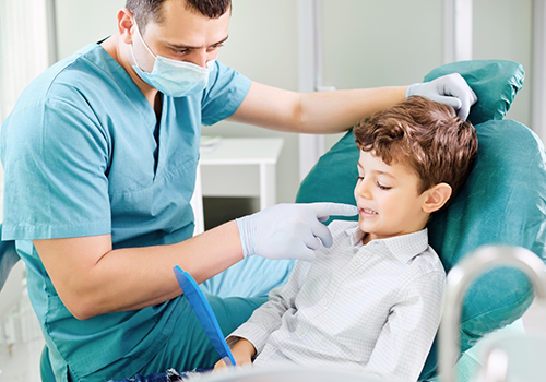 Young boy in the dental chair looking at his teeth in a mirror