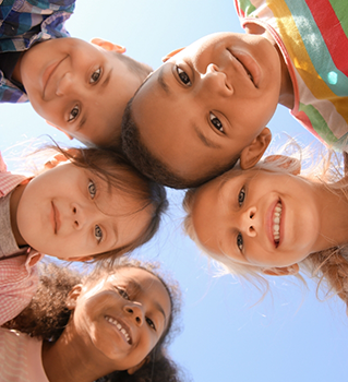Several kids standing in a circle with their heads together in the middle looking down at the camera
