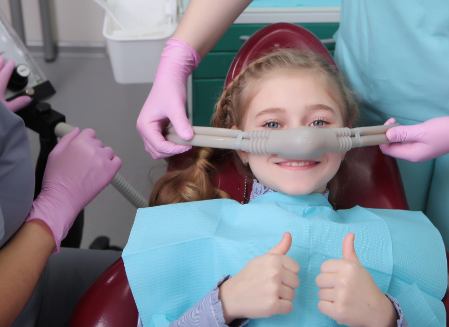 Little girl giving thumbs up with dental sedation mask on